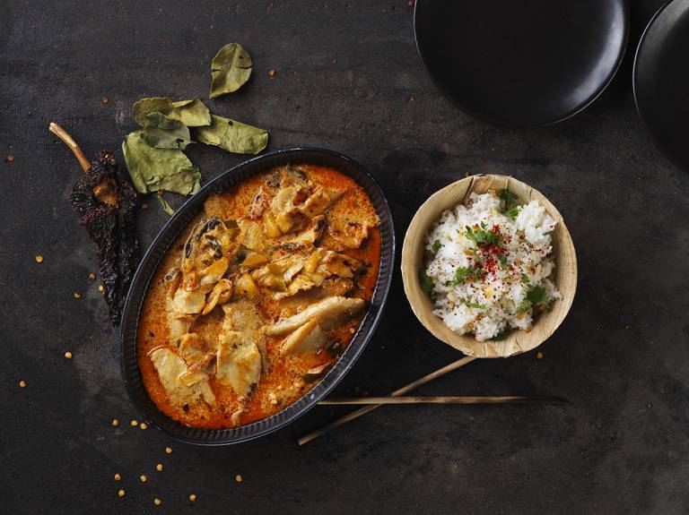 Vegansk röd curry i en gryta bredvid en skål ris på ett svart bord
