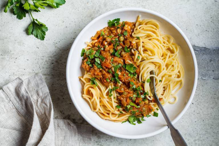 Vegansk bolognese på linser med spaghetti i en vit tallrik på ett bord