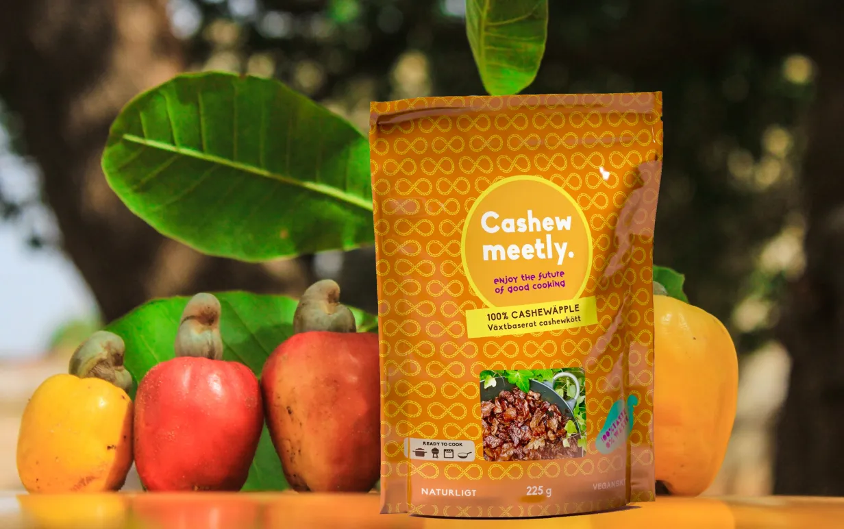Cashewmeetly i förpackning med cashewäpplen och grönska i bakgrunden.