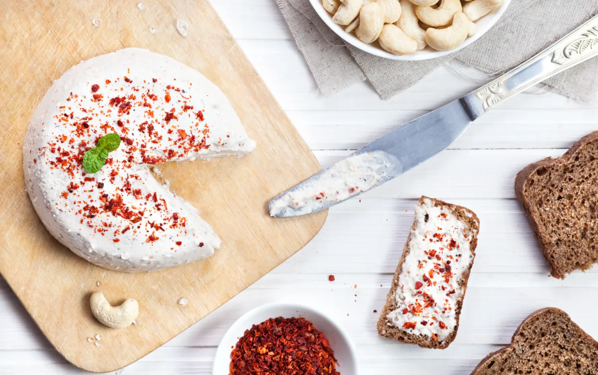 Vegan rå ost från cashewnötter sprids på brödet med kniv på den vita träbakgrunden