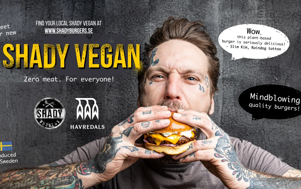 Tatuerad man som äter en vegansk hamburgare mot en mörk bakgrund