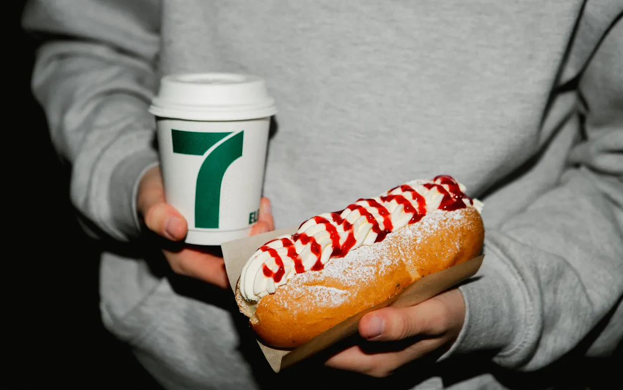 Man som håller en pappmugg med kaffe i andra handen och en semmelbakelse i korvbröd i den andra