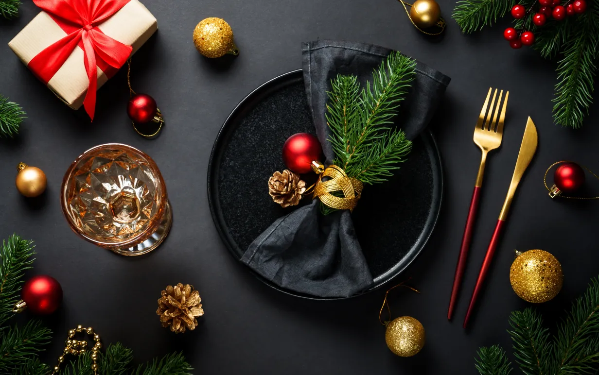 Christmas table setting with black plate, wine glass, cutlery and holidays decorations.