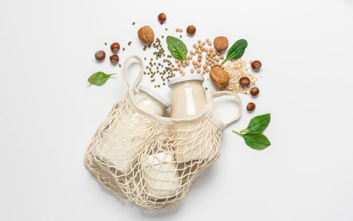 Variety of vegan plant based milk in zero waste mesh bag. Top view of lactose free milk based on nuts, legumes, oatmeal on white background
