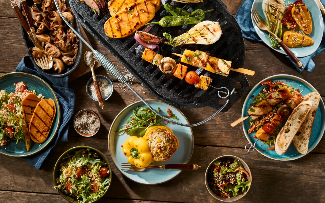 A vegetarian barbecue grill and various gourmet dishes on a rustic timber table.