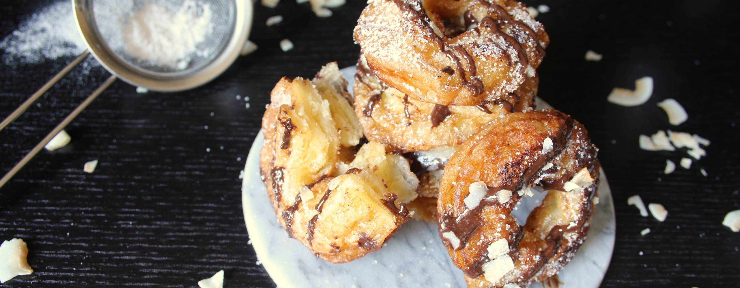 Cronuts med choklad och kokosflarn på ett vitt fat på ett mörkt bord