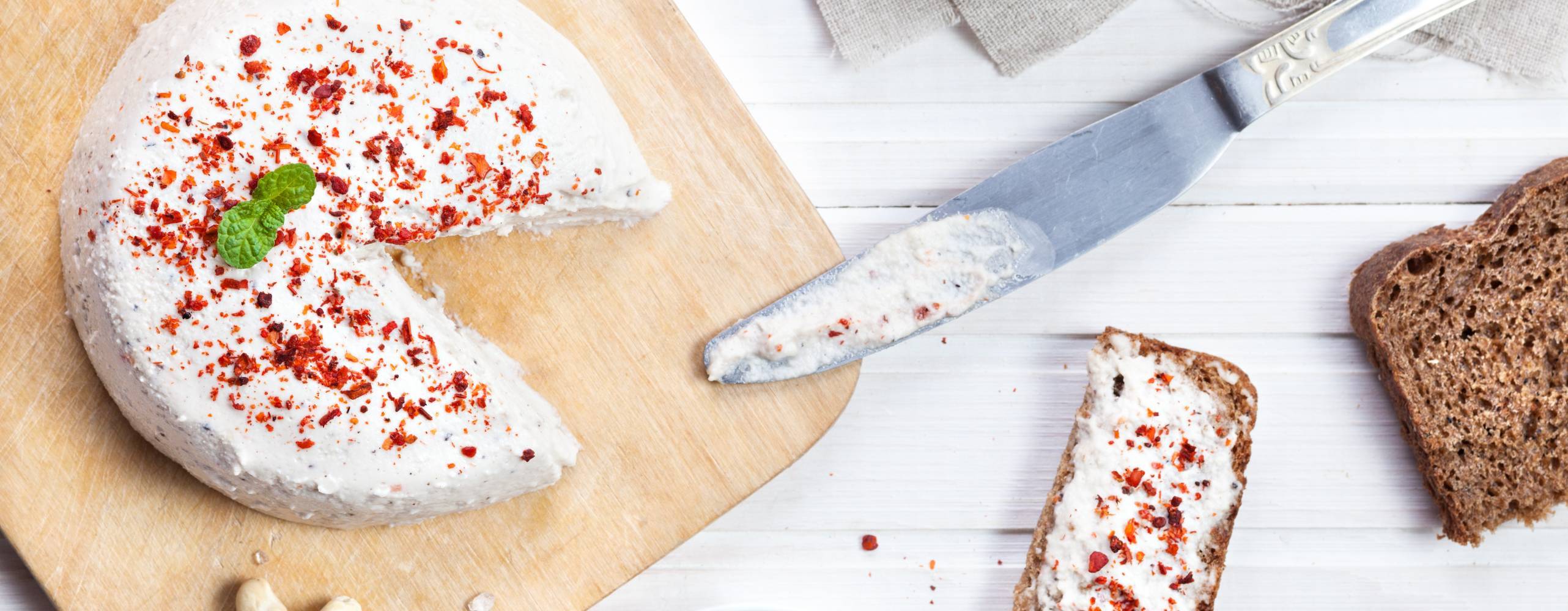 Vegansk cashewost toppad med chiliflingor på en skärbräda.