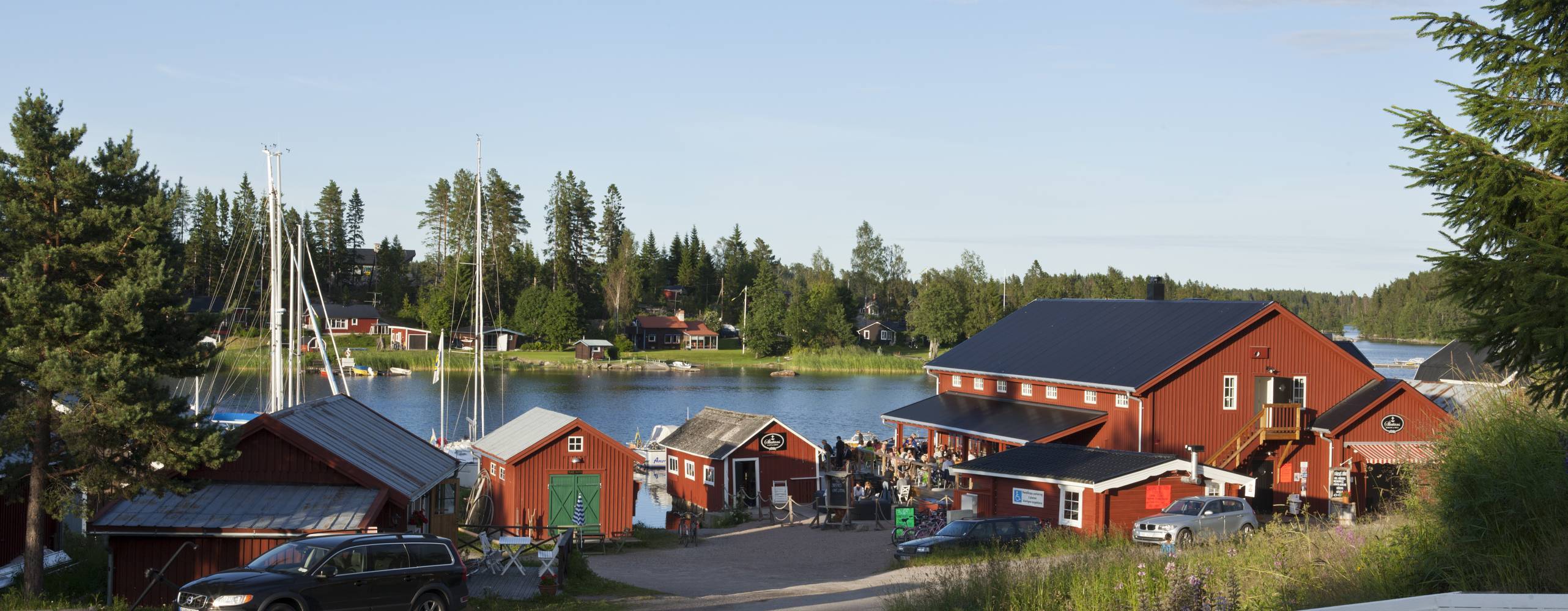 View of several red buildings in evening lit on July 17, 2012 in Jungfrukusten, Sweden. Gravel road, wooden fence, bridge and a Restaurant.