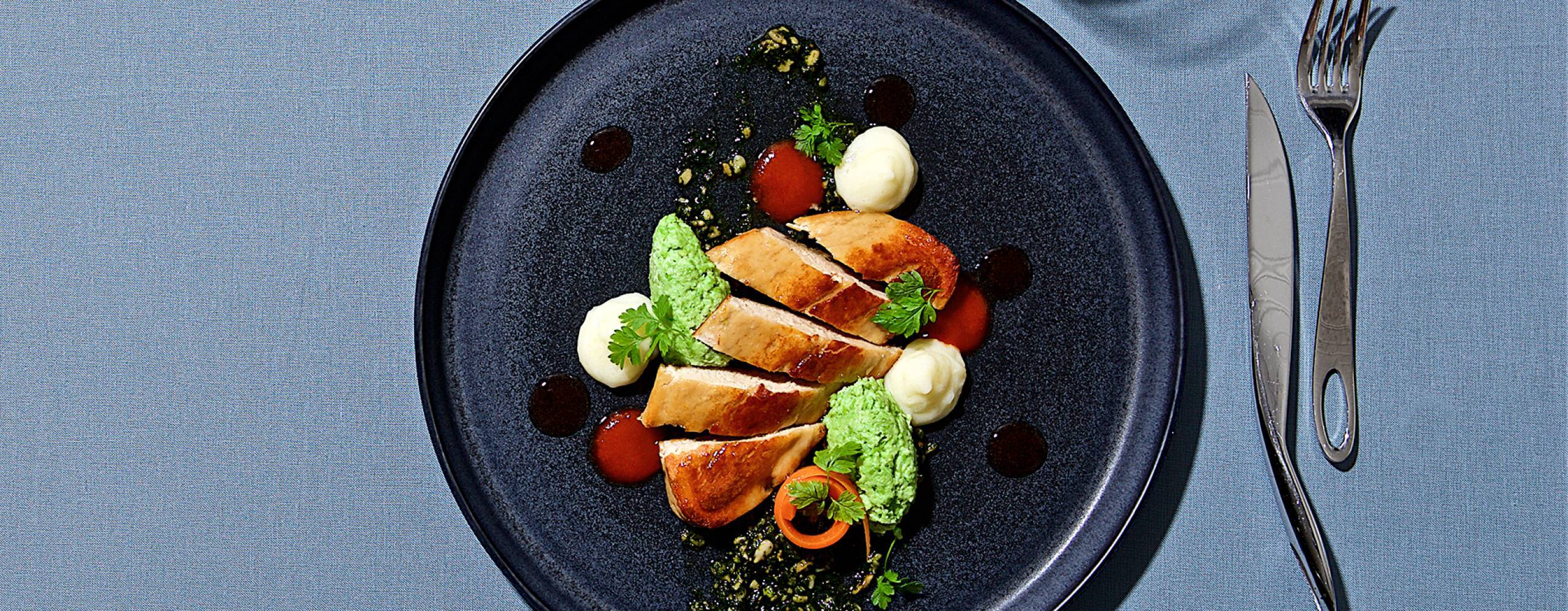 Vegansk quornfilé på tallrik med bestick och vattenglas runtom, fotat ovanifrån mot blå bakgrund.