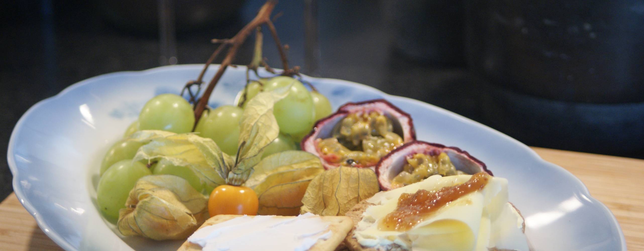 Vegansk ostbricka med kex och frukt. I bakgrunden skymtas två vinglas.