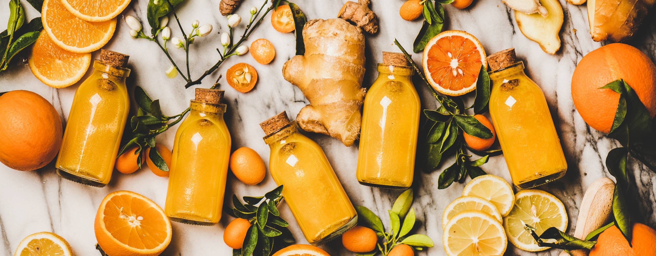 Apelsin, ingefära och små flaskor med apelsinjuice, utlagt över yta.