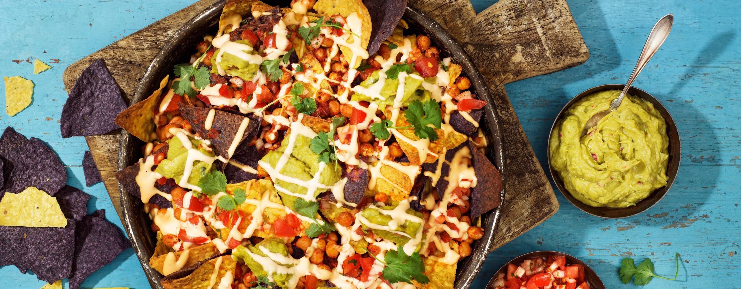 En tallrik med nachos på en skärbräda i trä som står på ett turkost träbord