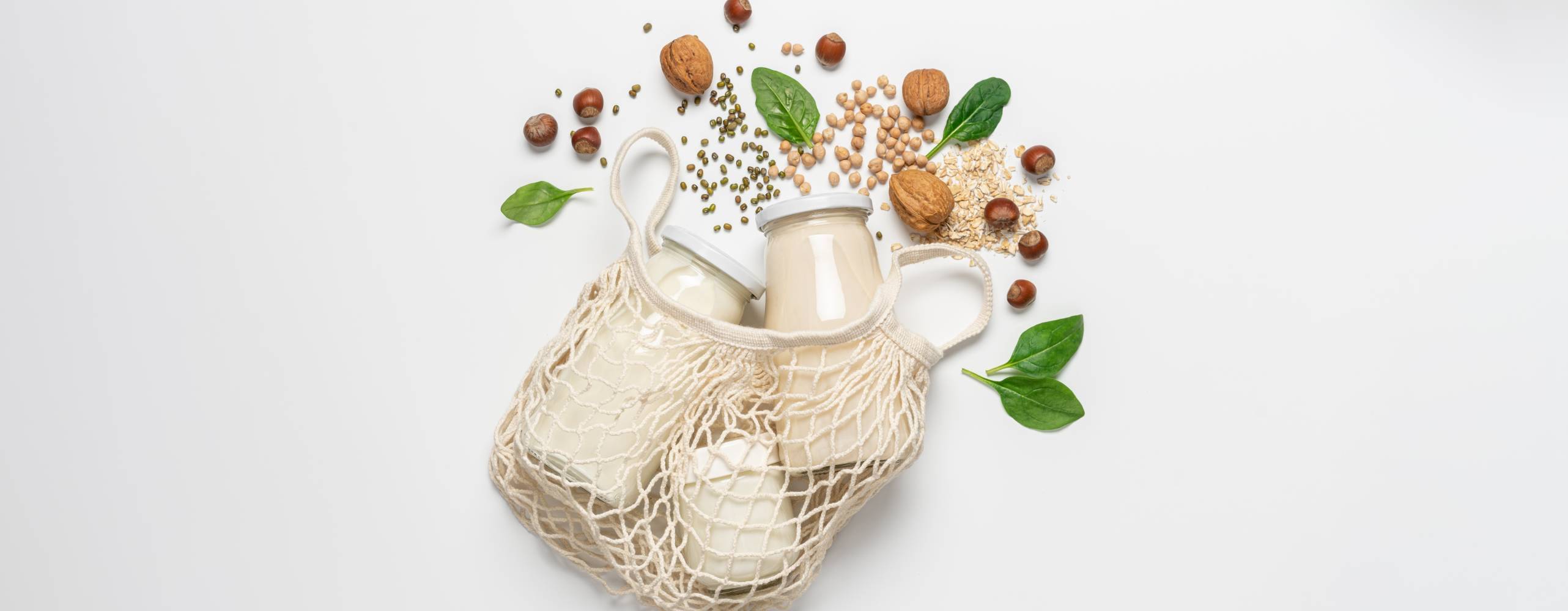 Variety of vegan plant based milk in zero waste mesh bag. Top view of lactose free milk based on nuts, legumes, oatmeal on white background