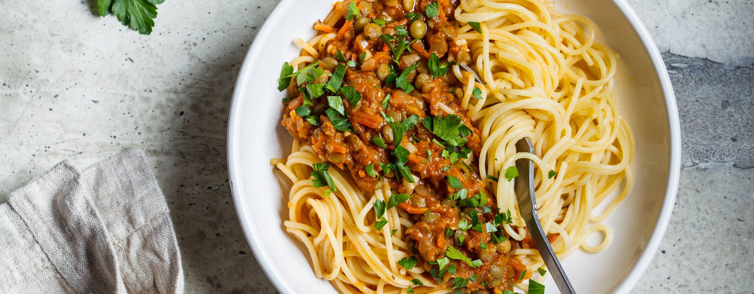 Vegansk bolognese på linser med spaghetti i en vit tallrik på ett bord