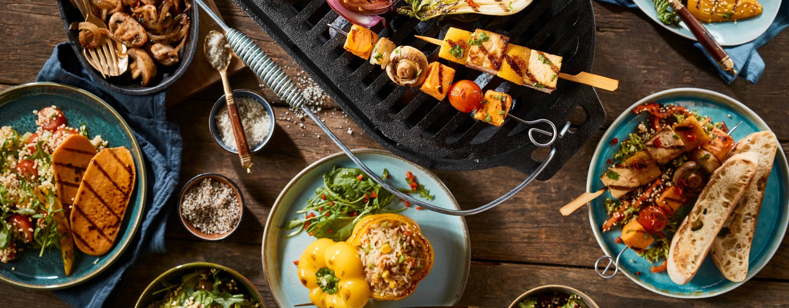 A vegetarian barbecue grill and various gourmet dishes on a rustic timber table.