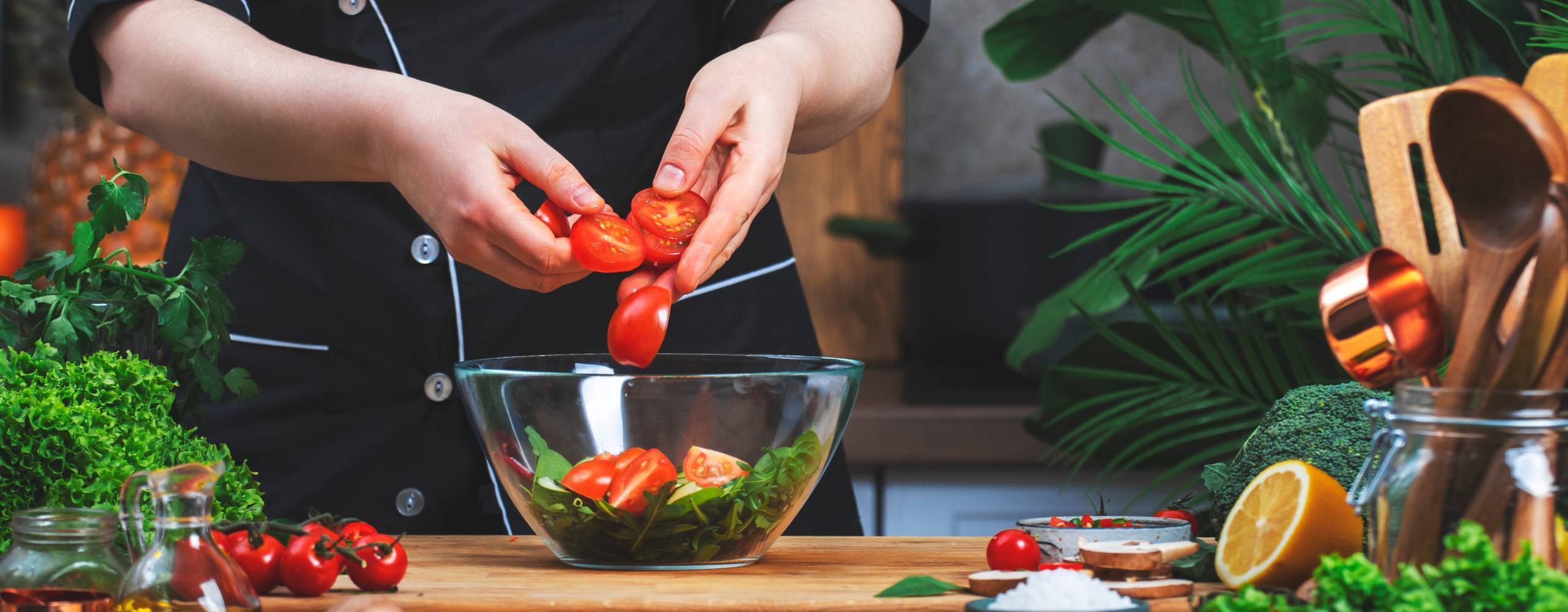 Matlagning i köket. Kocken lägger ​​tomater i skål med ruccola sallad. på träbord med köksredskap, grönsaker, örter och ingredienser. Hälsosamt veganskt ätande, recept, bloggande